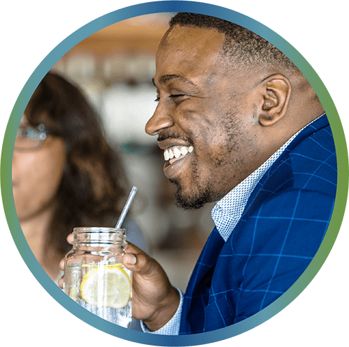 Picture in circle shape showing a black man wearing a blue suit drinking from a glass cup and a straw.